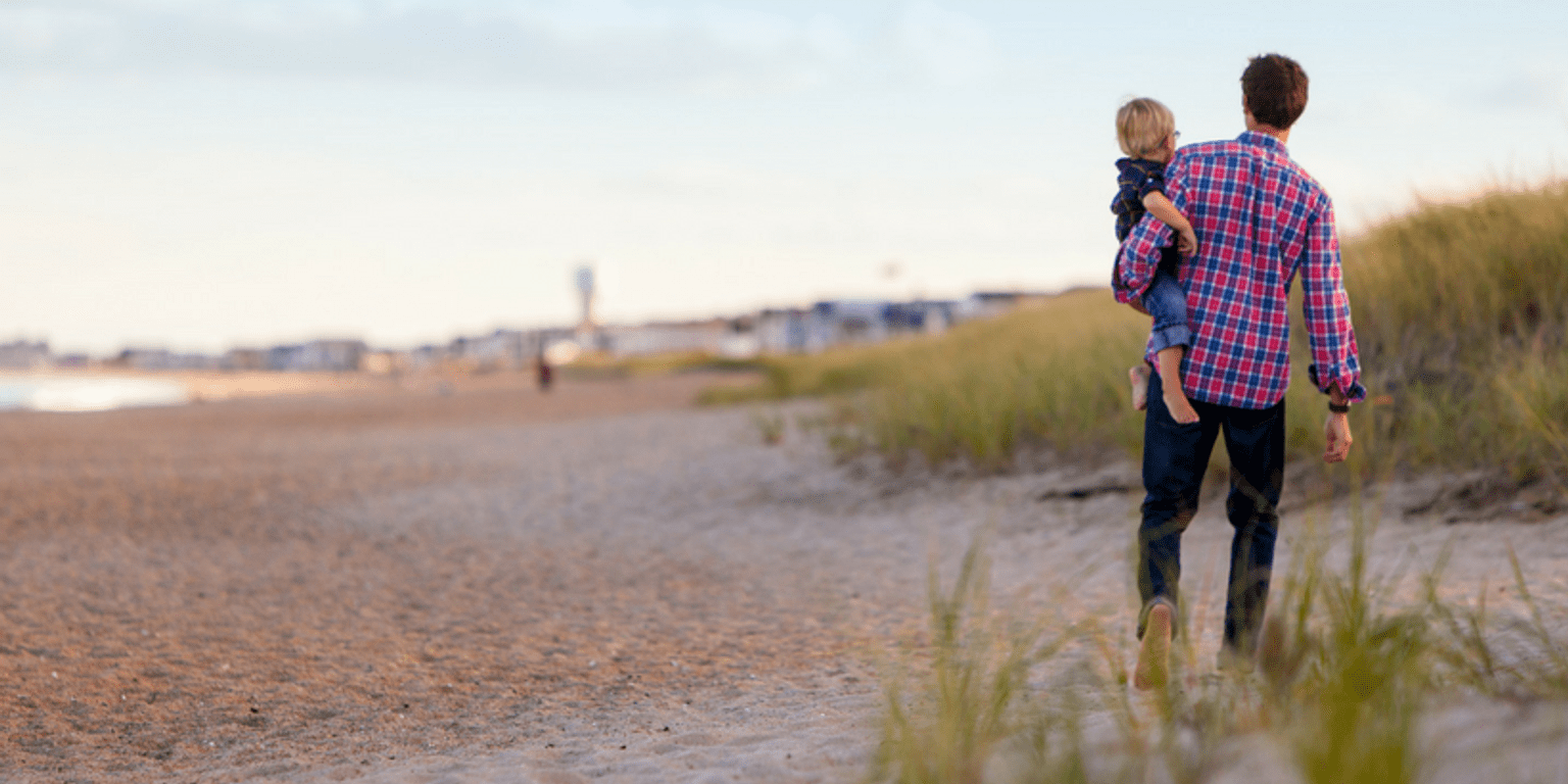 Father holding his child at the beach ""