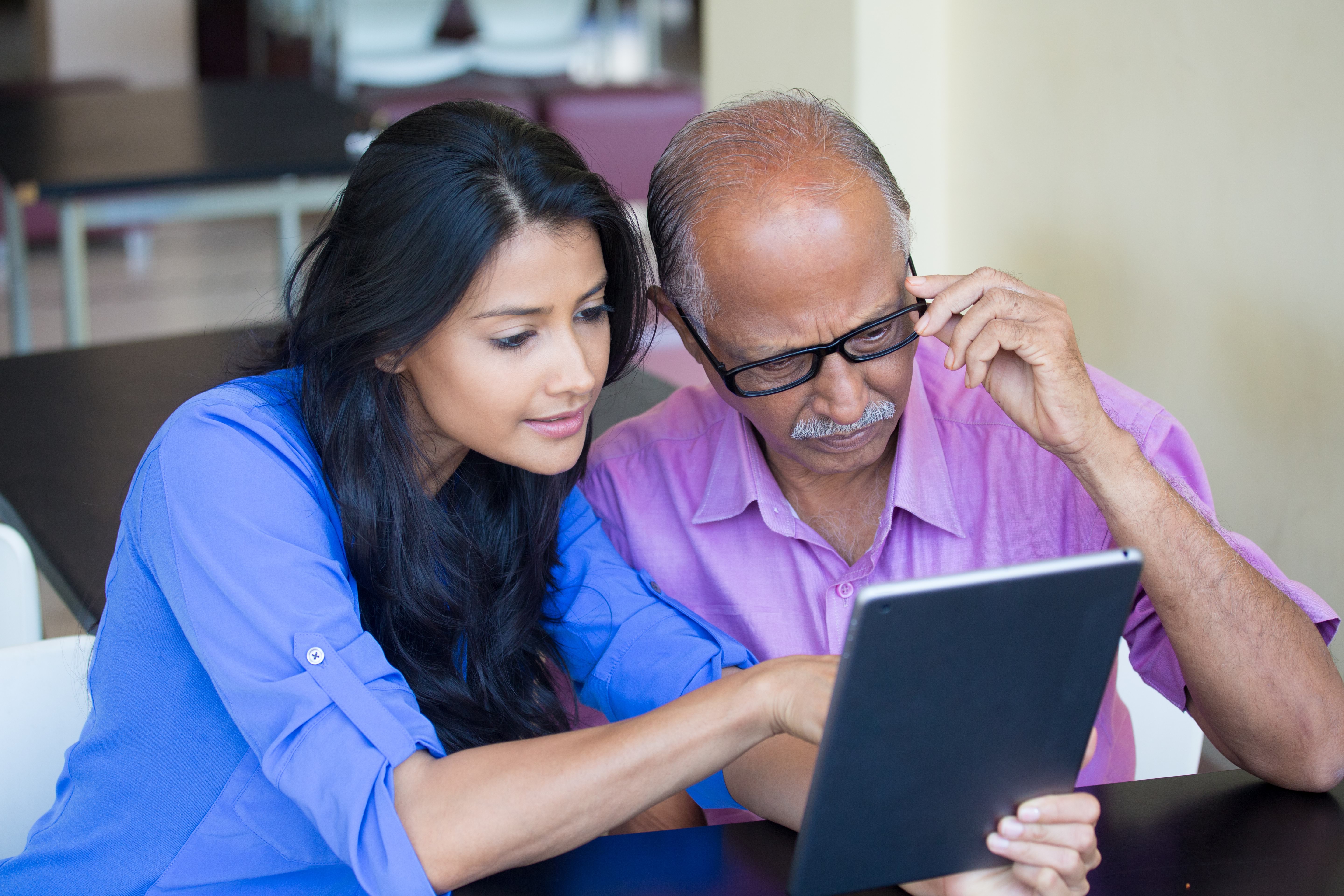 A young woman is pointing at a tablet screen while an older man is watching closely.