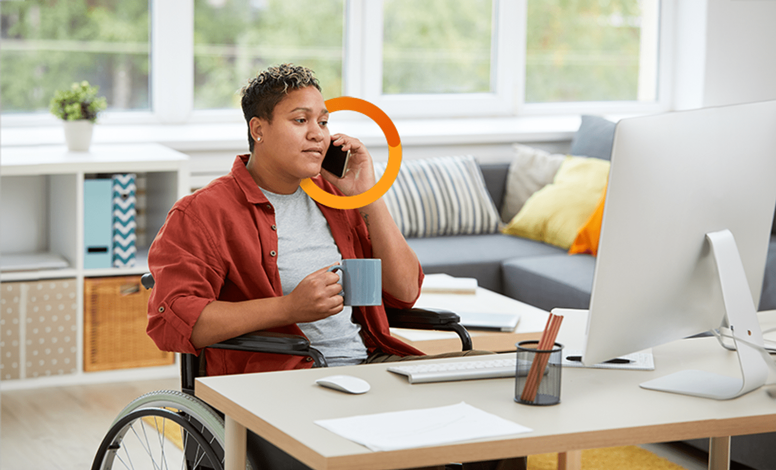 A woman is in her wheelchair at a desk, on the phone, with a computer in front of her