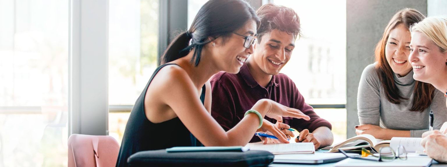 People sitting at a table smiling with books in front of them. 