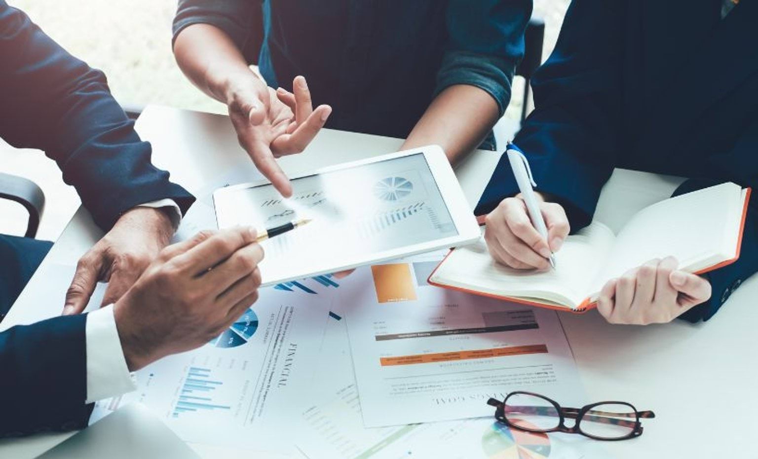 Three people looking at reports on a desk Three people looking at reports on a desk