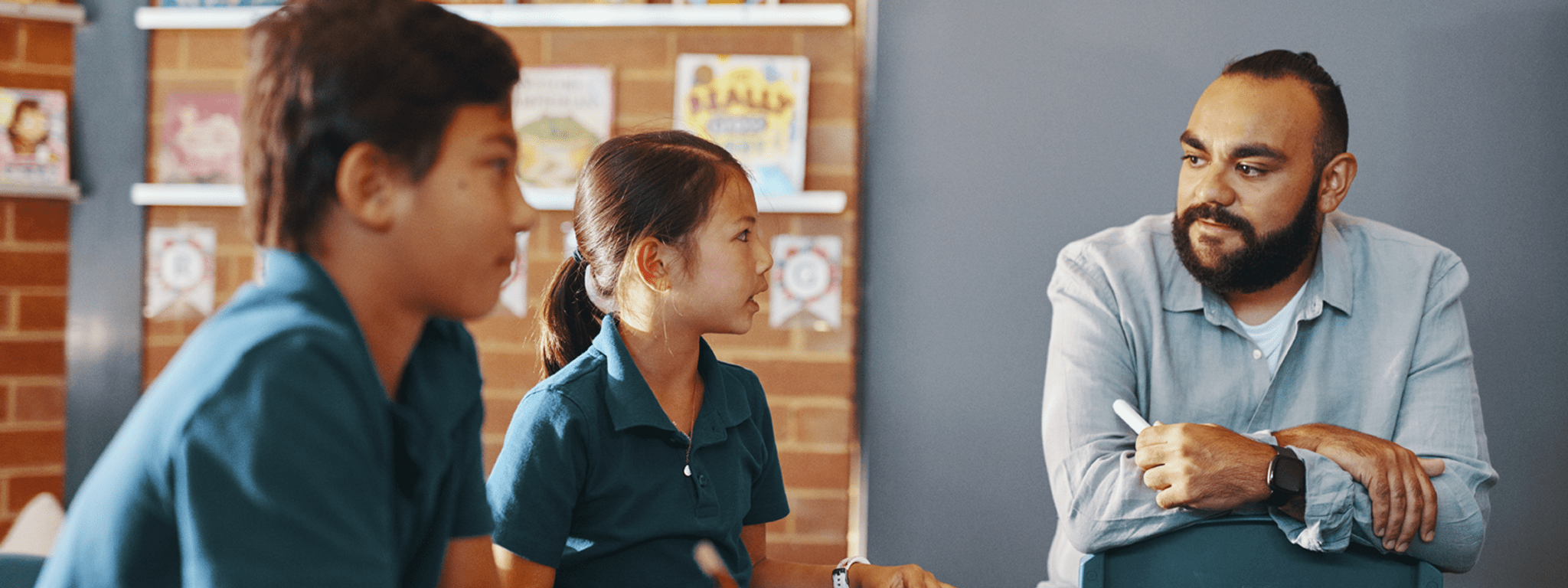 Male teacher in a blue shirt talking with two young students.