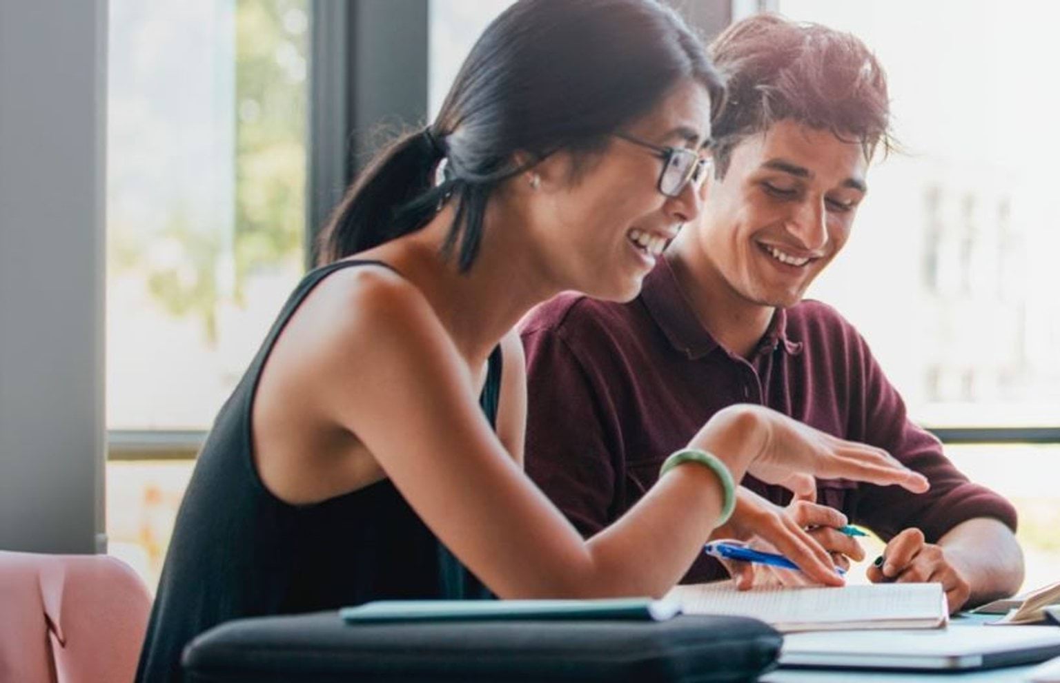 Two students sitting at a desk, holding pens and smiling.