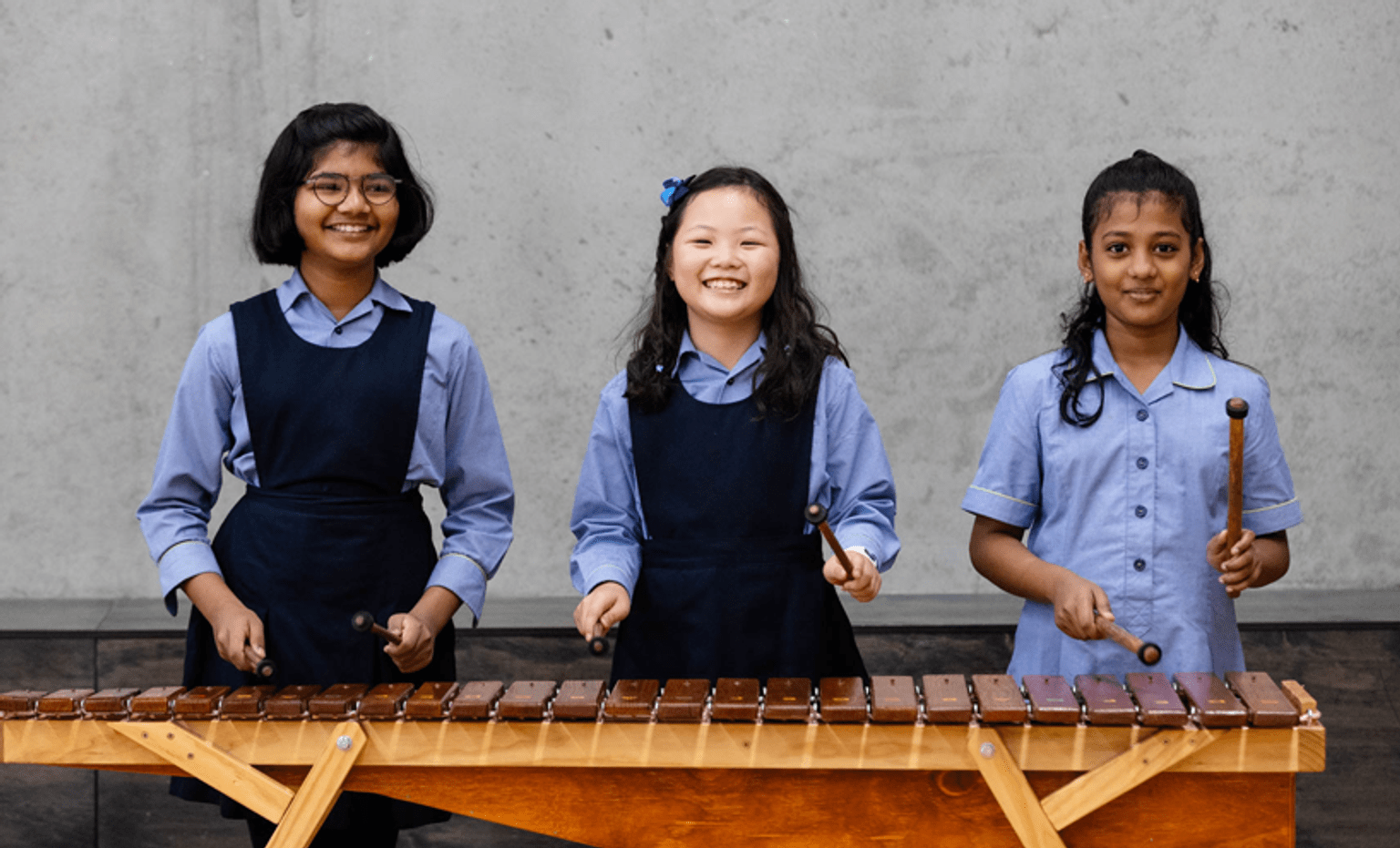 Schools card Three girls in school uniform smile and play marimbas.