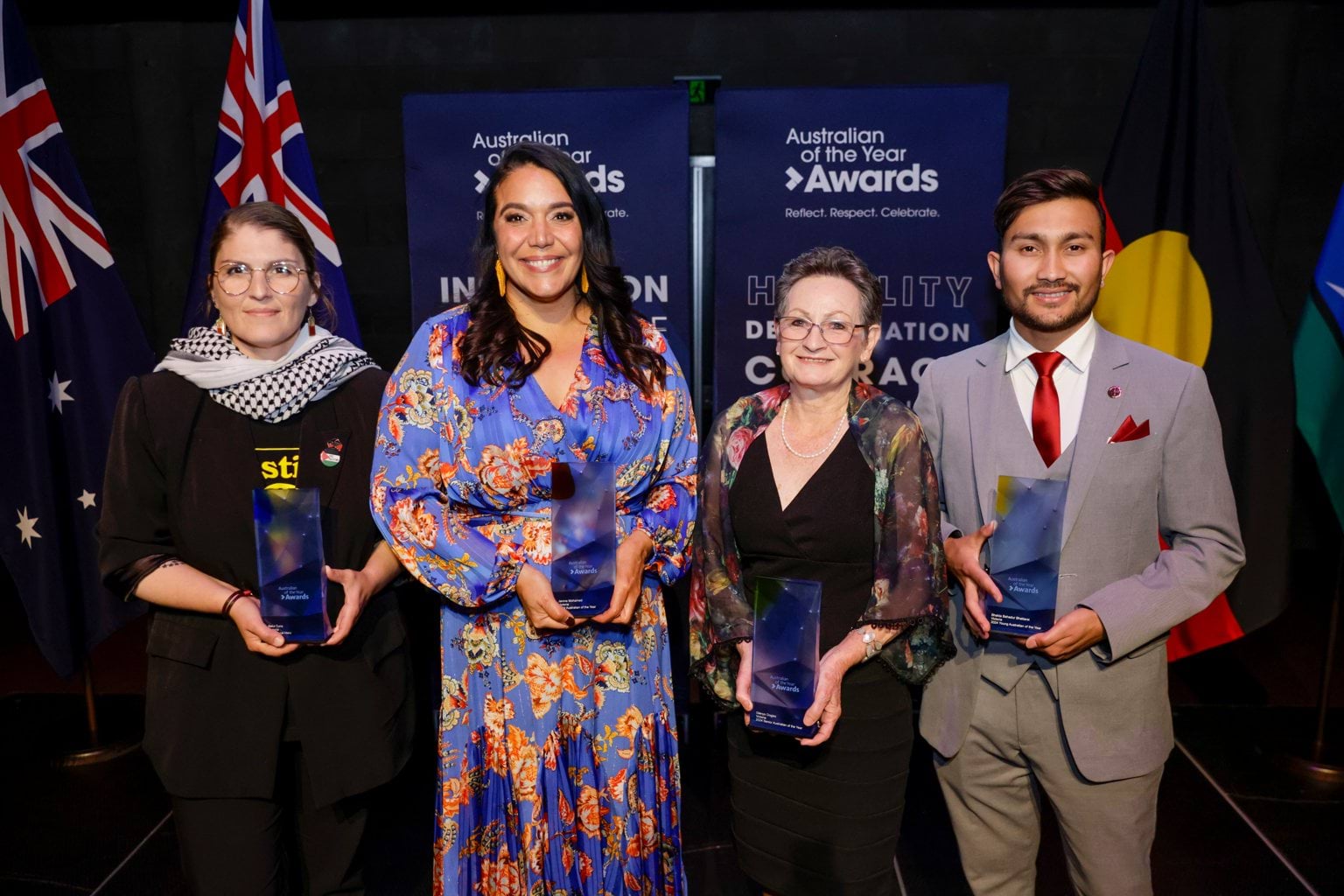 2024 Victorian Australian of the Year Awards Four people stand near flags each holding an award