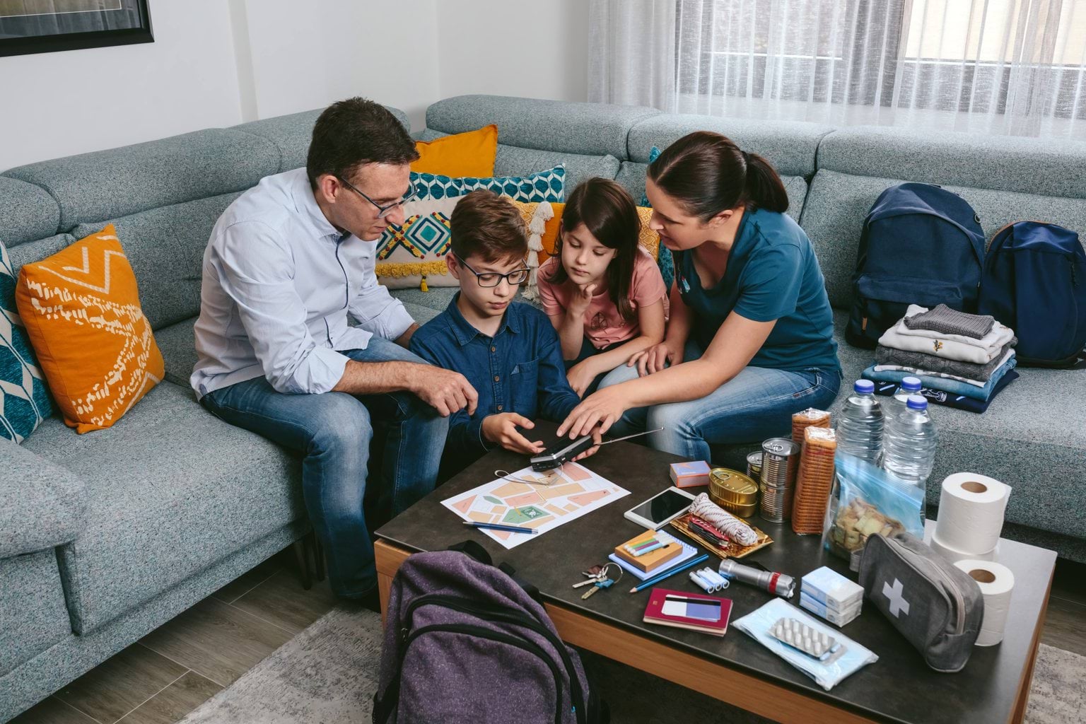 Family meeting for emergency preparation A fathher mother and two children sitting down in front of first aid kit, planner, phones and torch