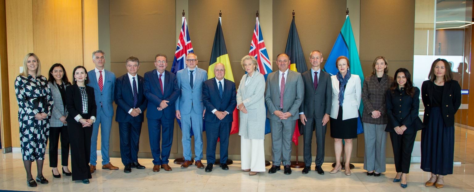 Princess Astrid of Belgium visit 2023 15 people stand in a row in front of 5 flags