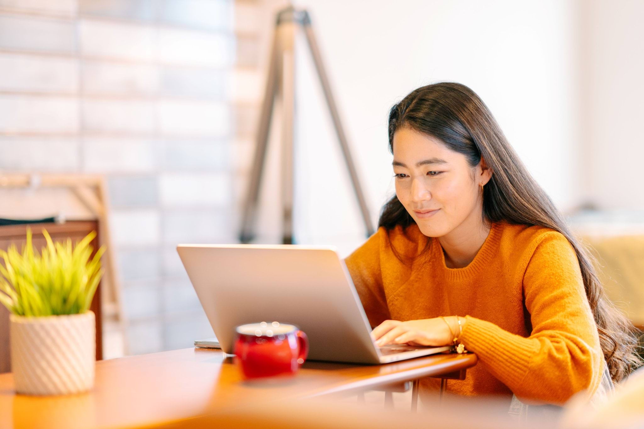 A student in an orange jumper looking at a laptop on a table.