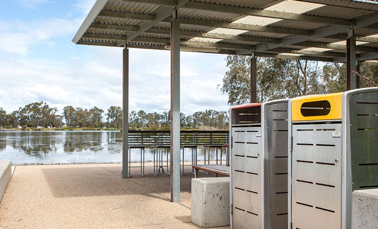 A barbecue area beside a lake, with waste and recycling bins in the foreground