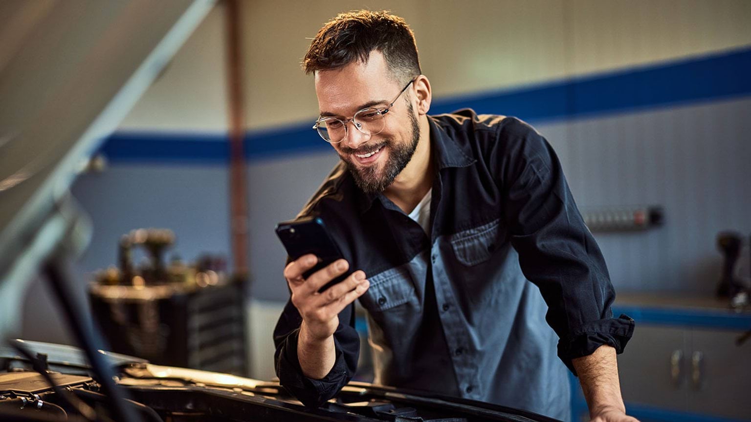 TAFE and Training Line person working on car engine looking at a mobile device