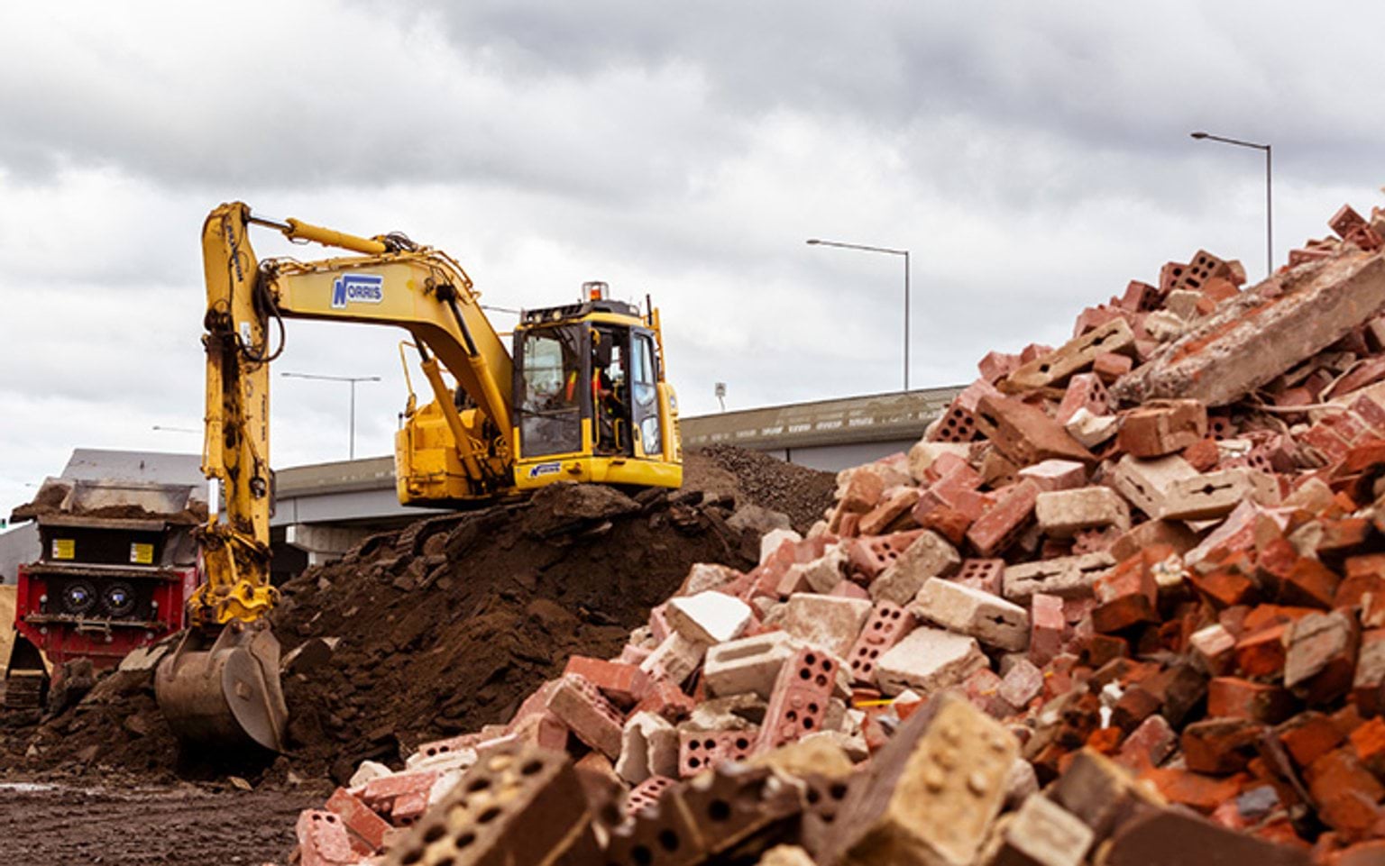 Excavator working a mound of recycled asphalt and brick.