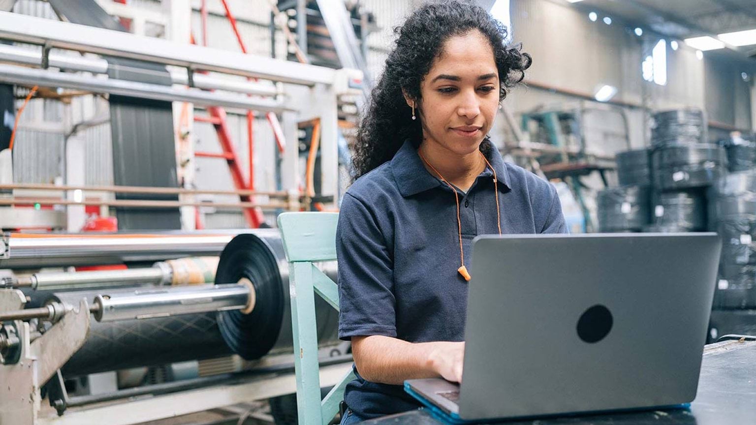 Woman working on laptop in factory or industrial setting.