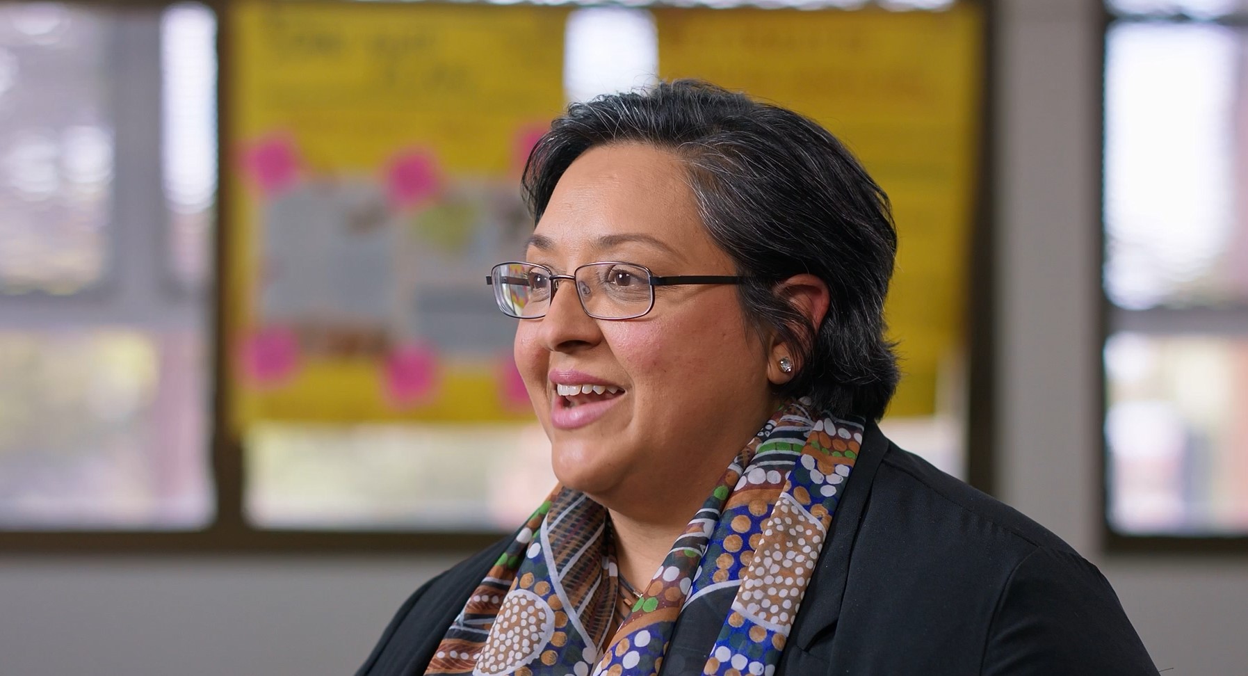 A smiling woman wearing glasses and a colourful printed scarf.