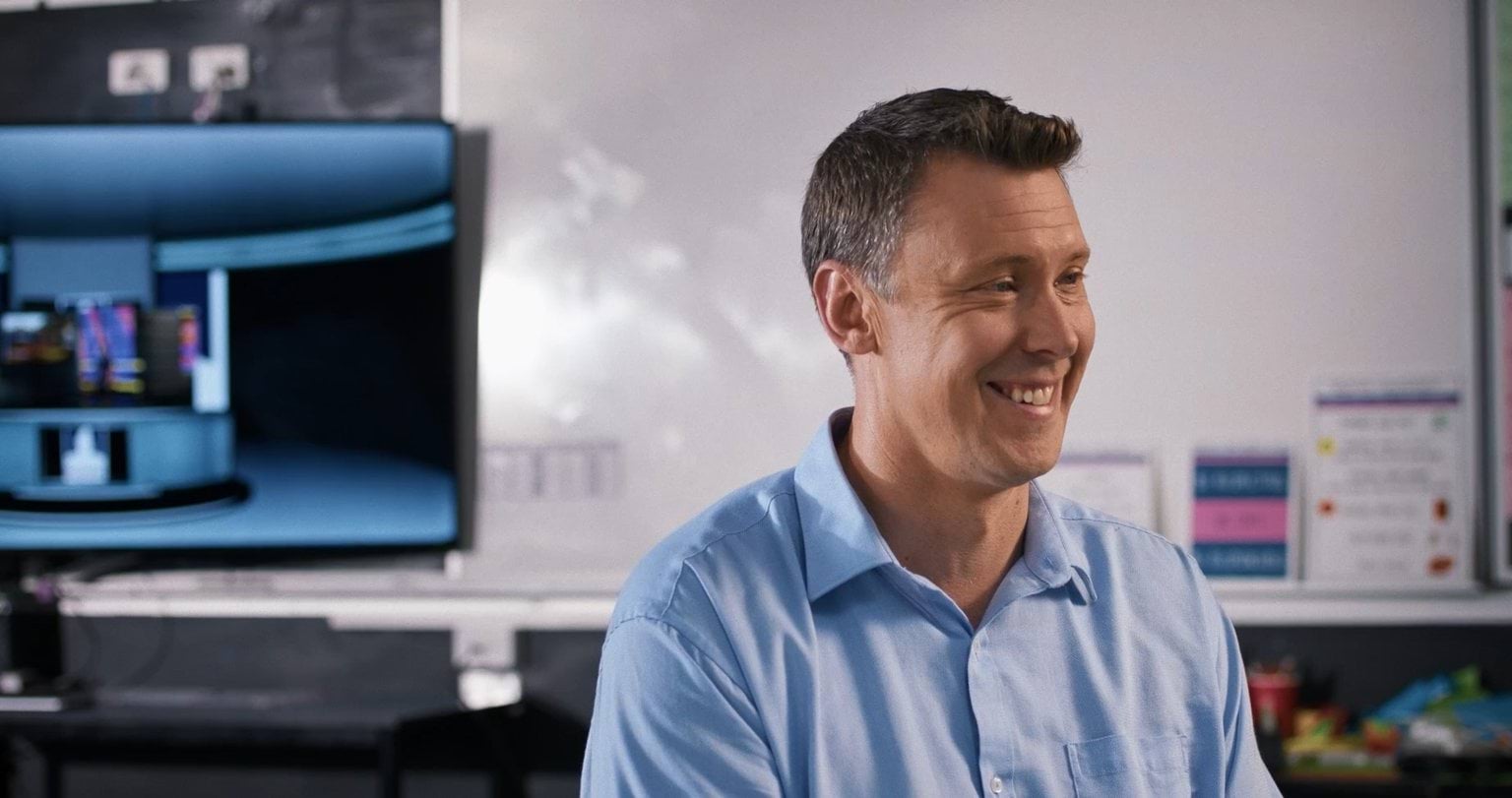 A man sitting in an office wearing a blue shirt.