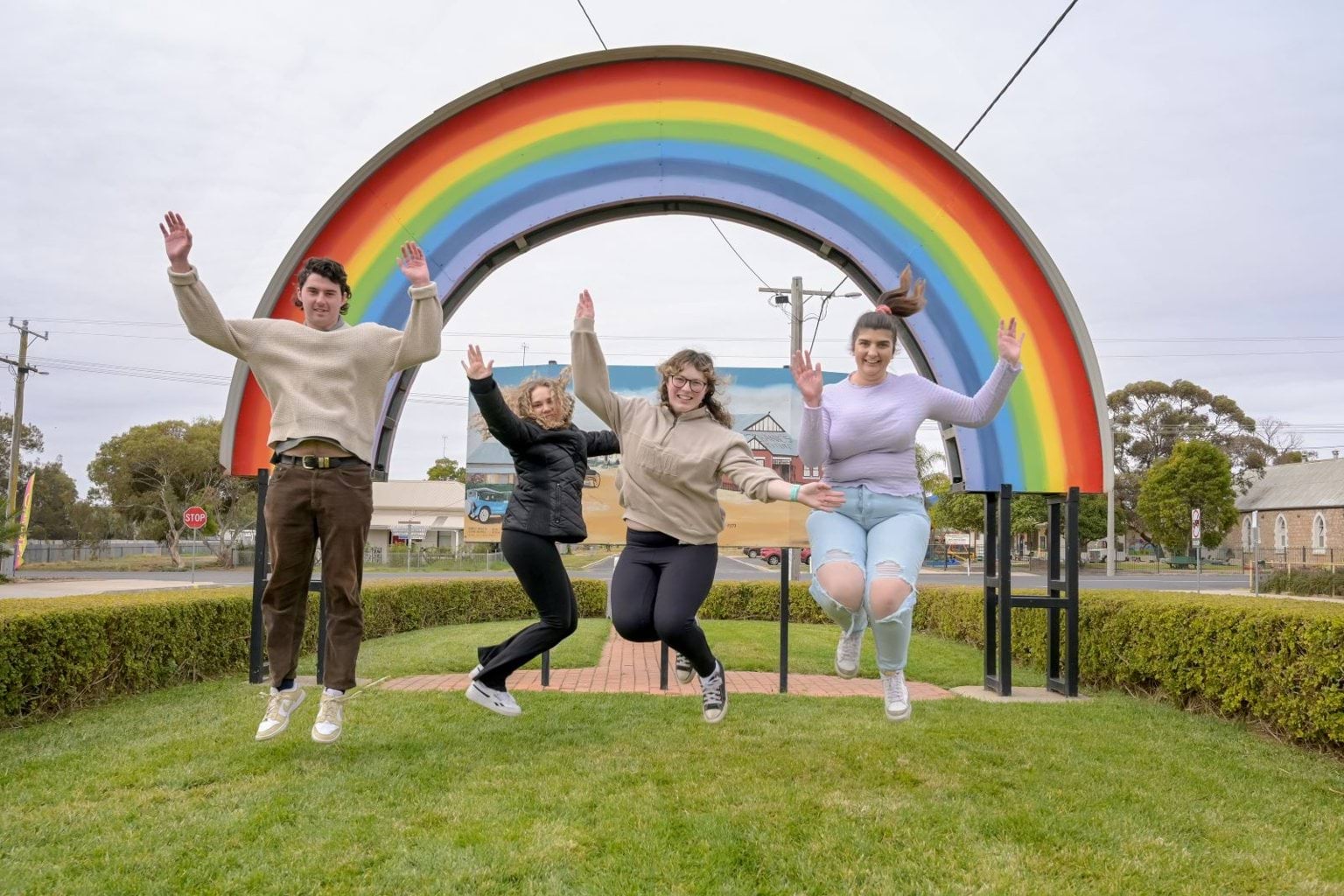 Four people jumping in the air in front of a large rainbow arch.