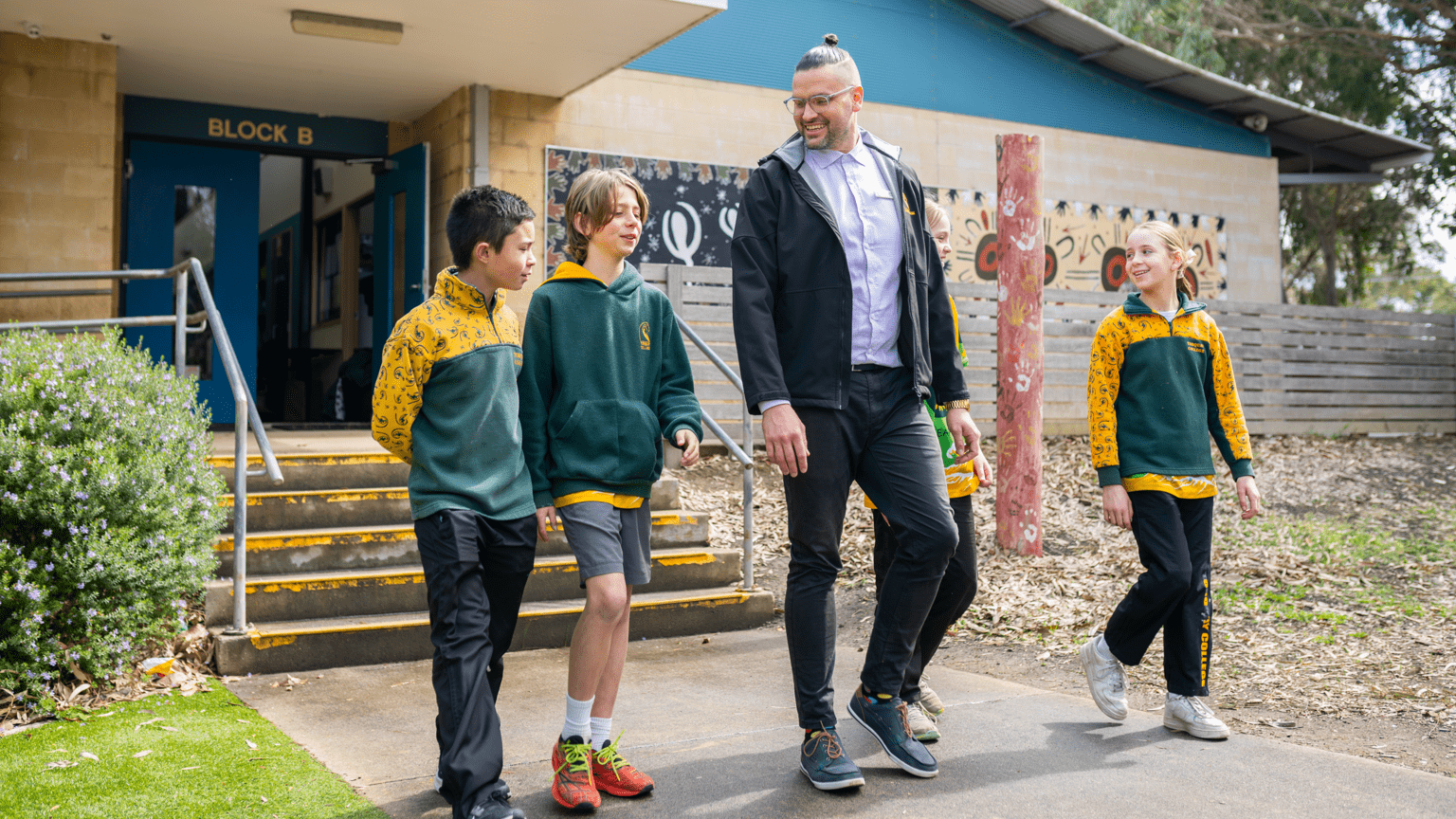 A man walking side-by-side 4 children in green and yellow jumpers.