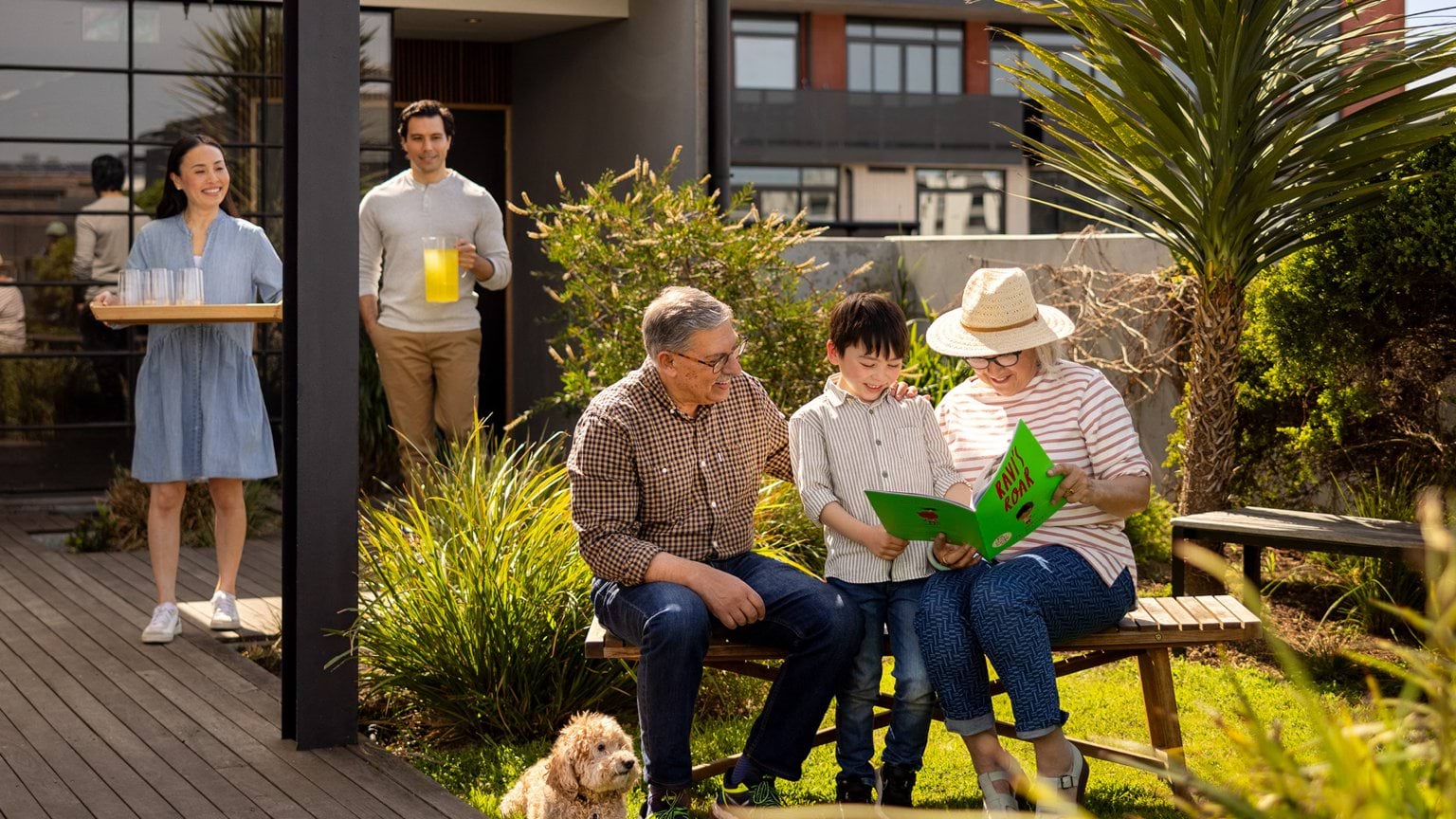 people sitting with a child looking at a book and couple walking up from behind