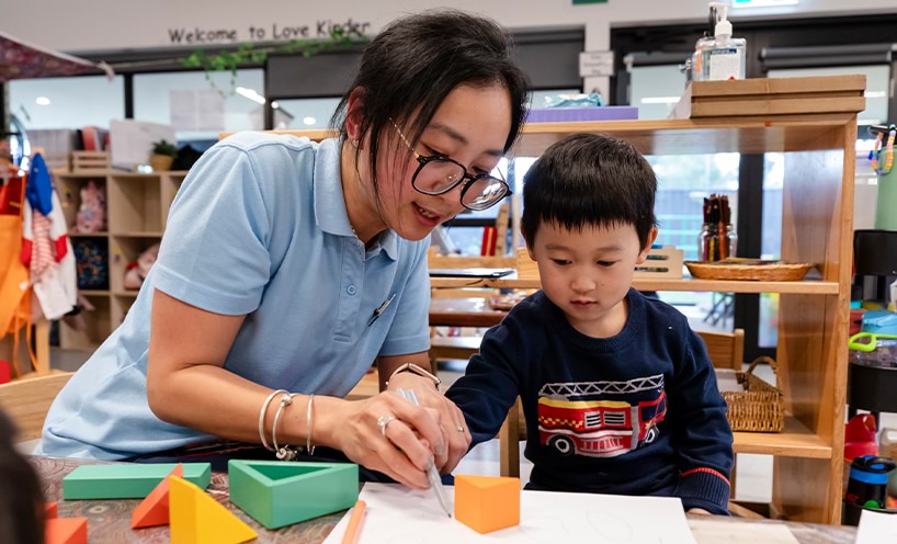 Educator and child tracing a triangular shaped block