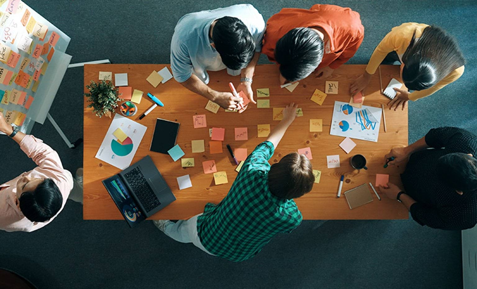 An aerial view of a group of people collaborating using sticky notes spread out on a table and whiteboard
