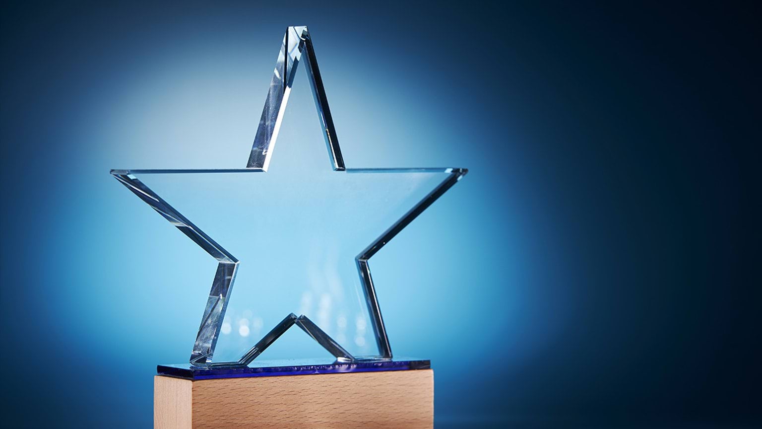 A star shaped trophy made of glass, illuminated on a dark blue background
