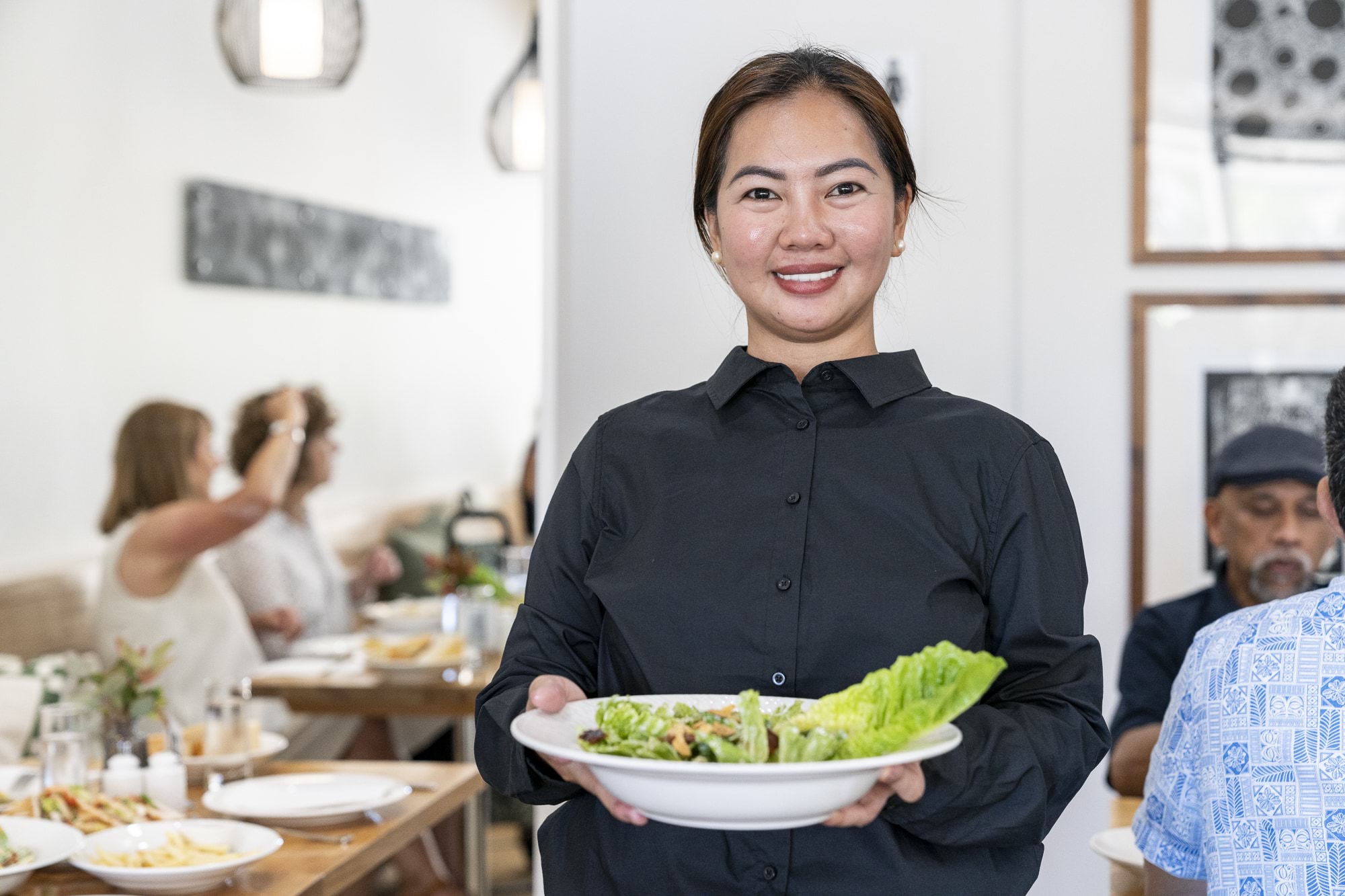 A smiling person carries a bowl of salad in a cafe.