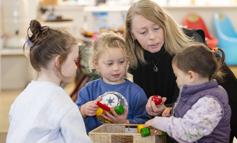 3 children playing with toys and an educator accompanying them