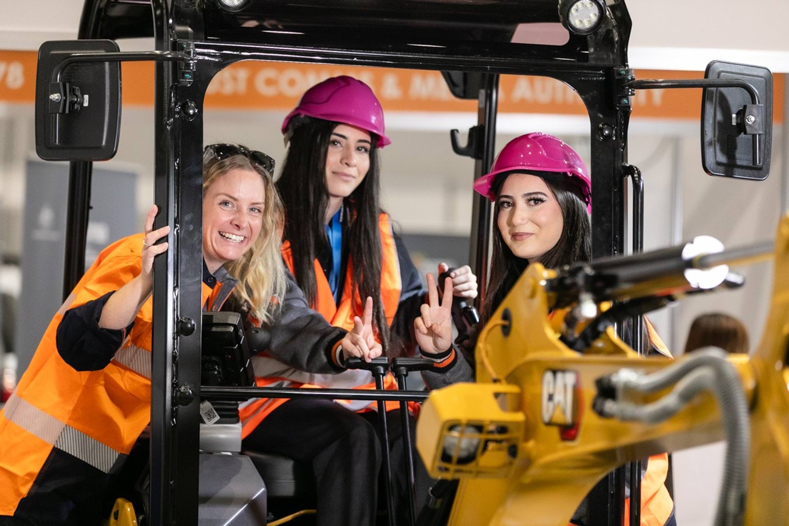 Female students posing with a female tradesperson on an excavator