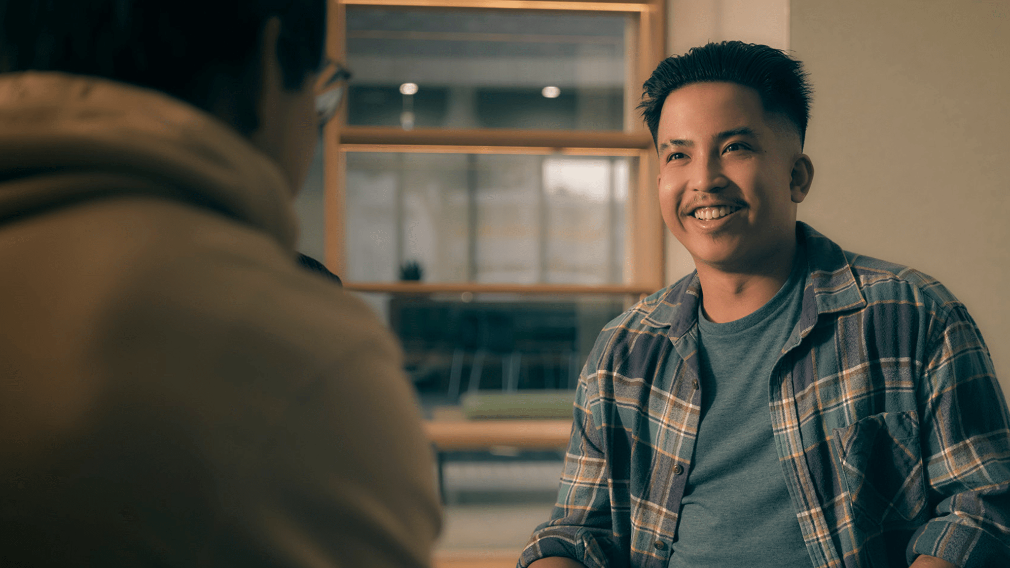 A person smiling and talking to someone with their back to the camera.